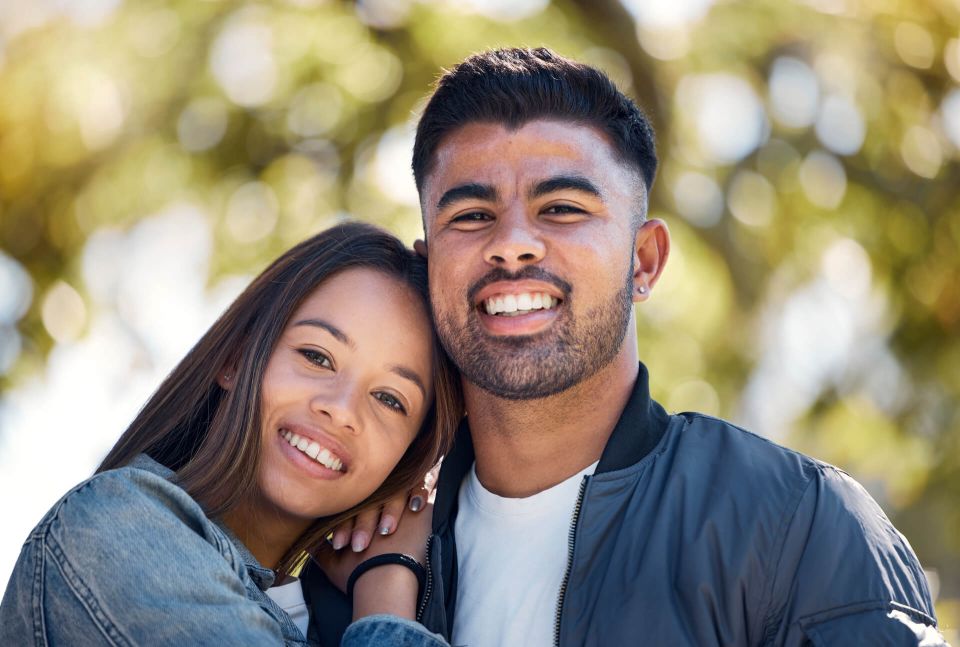 Pareja joven sonriendo abrazada al aire libre